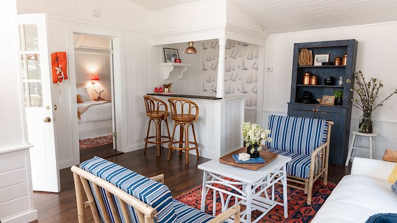 A cozy living room with nautical-themed decor, featuring striped furniture, a coffee table, and a small bar area with stools. End of sentence.