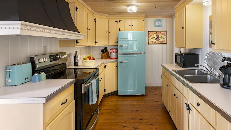 A cozy kitchen with yellow cabinets, a blue retro fridge, matching appliances, and wooden floors, creating a warm and nostalgic atmosphere.