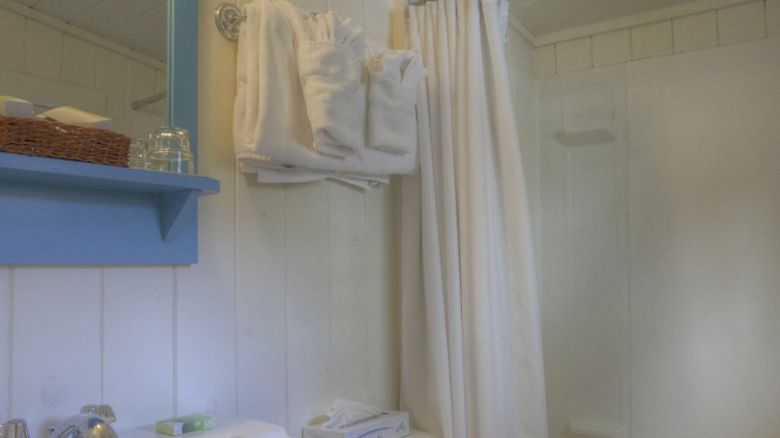 This image shows a small bathroom with a sink, mirror, and toilet on the left, a bath/shower combination with a curtain on the right, and towels hanging.