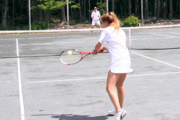 Two people are playing tennis on an outdoor court; one is about to hit the ball with a forehand shot, and the other is at the opposite end.