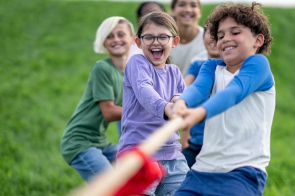 A group of children is playing tug-of-war, smiling and having fun on a grassy field.