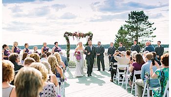 A bride and groom walk down the aisle outdoors, surrounded by guests seated on either side and a floral arch in the background, ending the sentence.