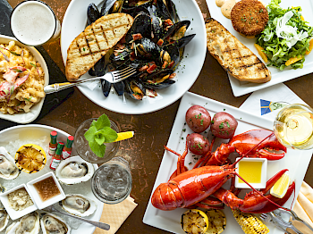 An assortment of seafood dishes including oysters, lobster, mussels, fries, and drinks are arranged on a table, ending the sentence.
