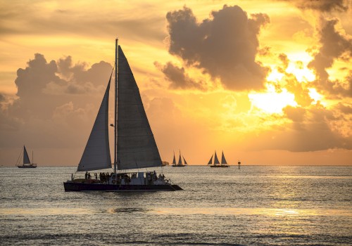 A sailboat on a calm ocean at sunset with other sailboats in the background and a dramatic sky filled with clouds, ending the sentence.
