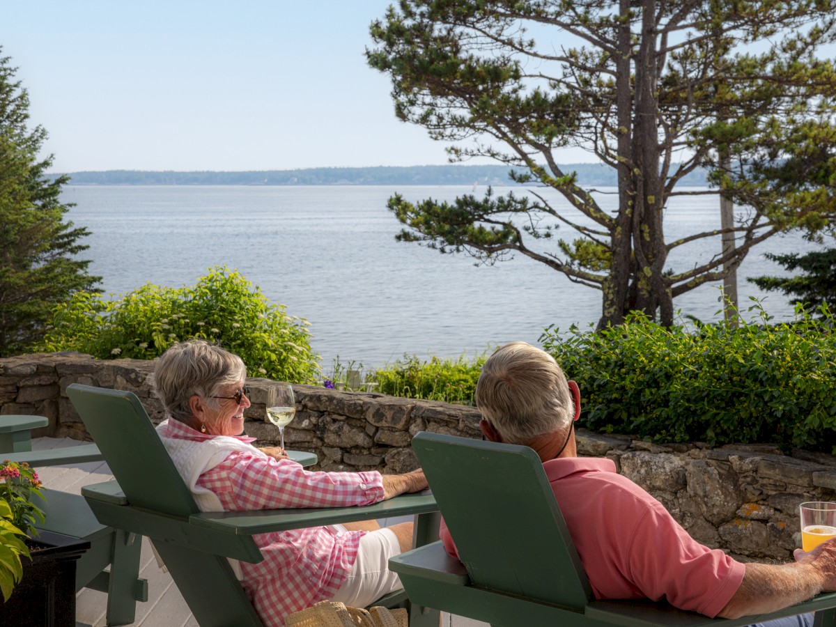 Two people relaxing in chairs with drinks, enjoying a scenic view of the ocean and trees.